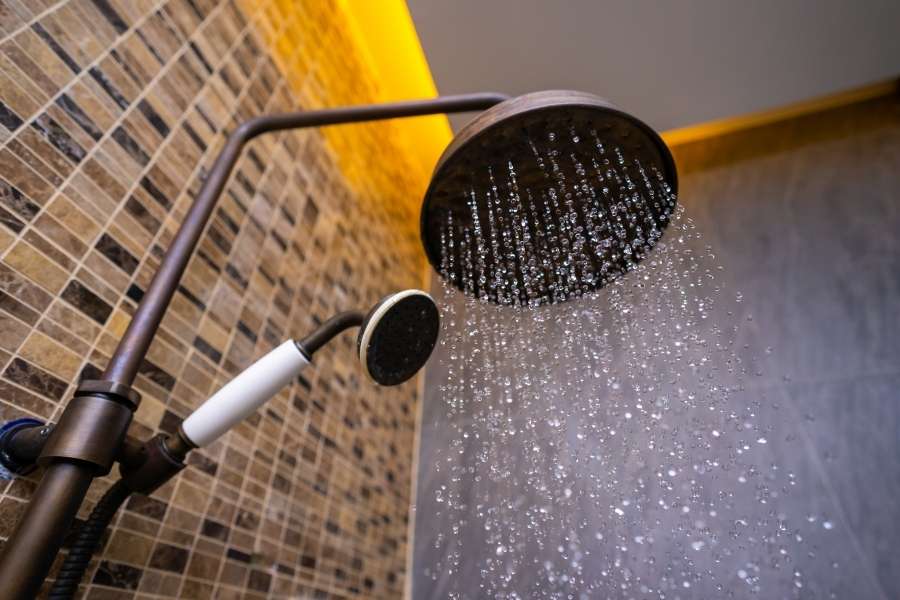 Système de douche bronze avec pomme de tête ronde et douchette à main sur fond de mosaïque dorée