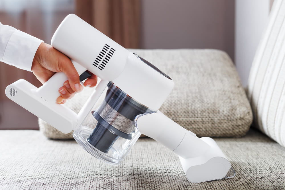 Gros plan sur un aspirateur multifonction sans fil utilisé pour nettoyer les miettes sur l'assise d'un canapé en tissu gris