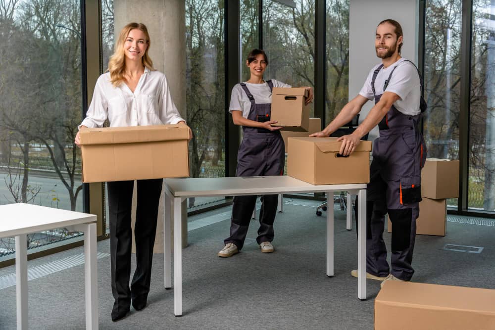 Une équipe de professionnels souriants porte des cartons dans des locaux neufs lors de la création d'une entreprise