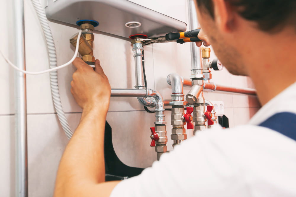 Gros plan sur un technicien utilisant une pince pour serrer les raccordements métalliques d'un chauffe-eau électrique mural afin d'éviter les pièges liés aux cinq mythes de plomberie