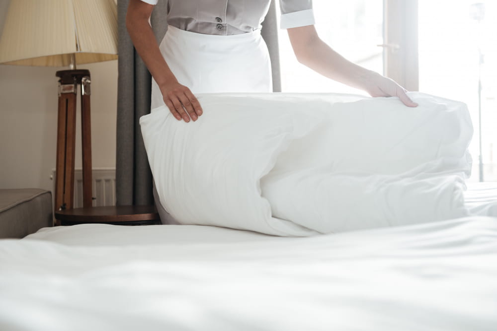 Une employée de maison change les draps blancs d'un lit d'hôtel pour maintenir une bonne hygiène de literie.