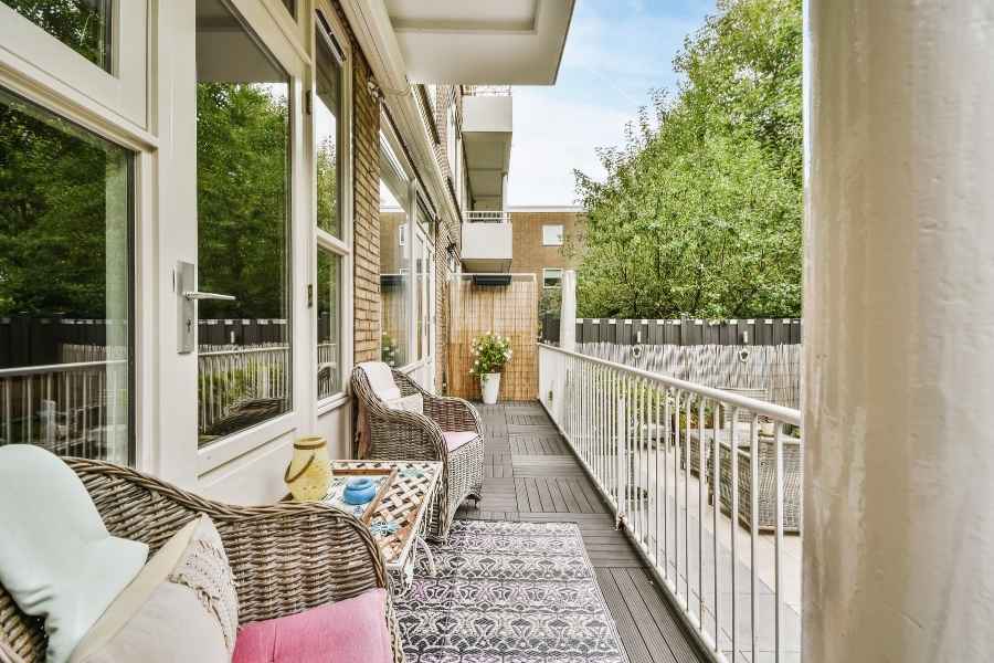Un long balcon filant aménagé avec des fauteuils en osier et un revêtement de sol en bois.