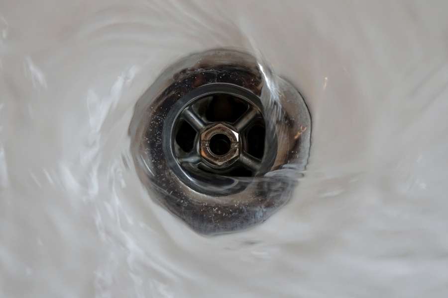 Gros plan sur l'eau qui s'écoule en tourbillon dans la bonde métallique d'un lavabo relié à un siphon de lavabo.
