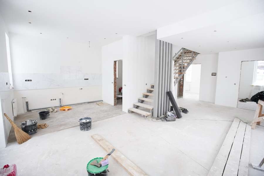 Intérieur d'un appartement en rénovation totale à Paris avec des murs blancs, des matériaux de construction au sol et un escalier en bois et métal en cours d'installation.