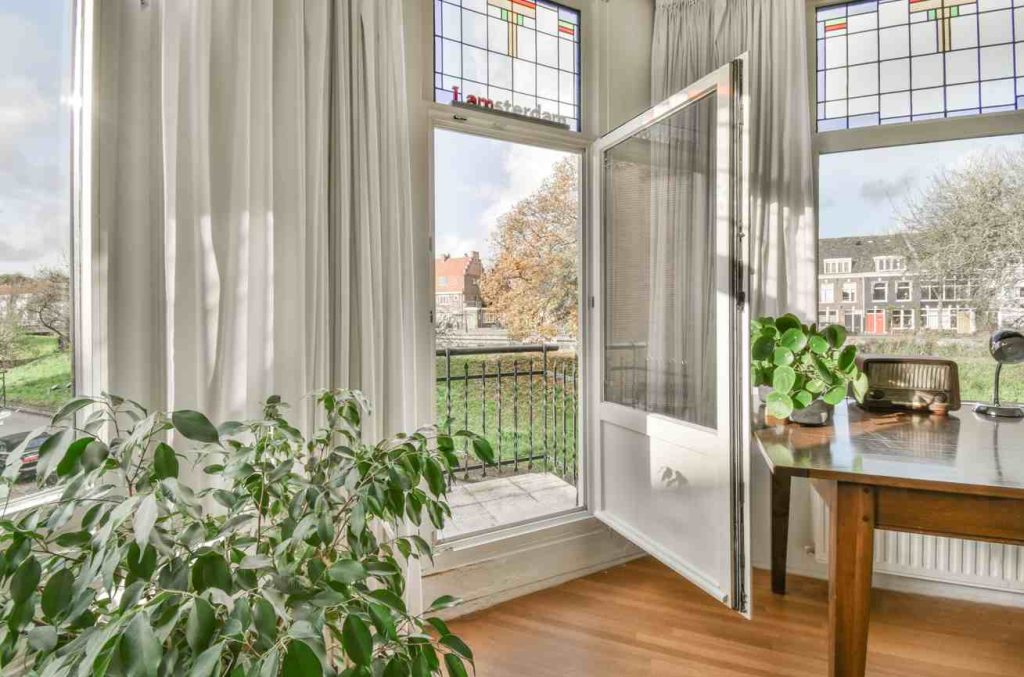 Intérieur lumineux donnant sur un balcon avec des plantes vertes et une porte-fenêtre sans trace de condensation.