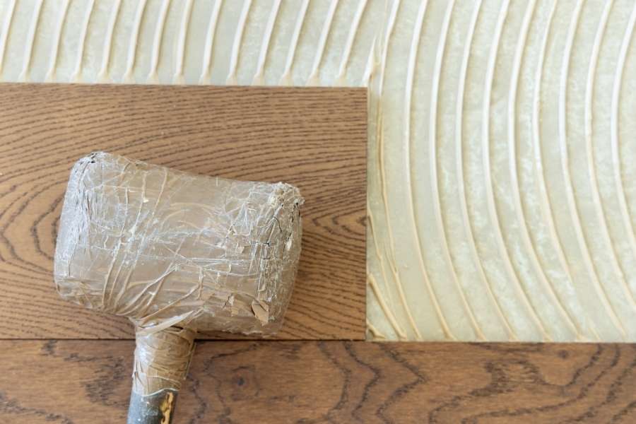La pose de lames de parquets en bois sur une couche de colle fraîche avec un maillet