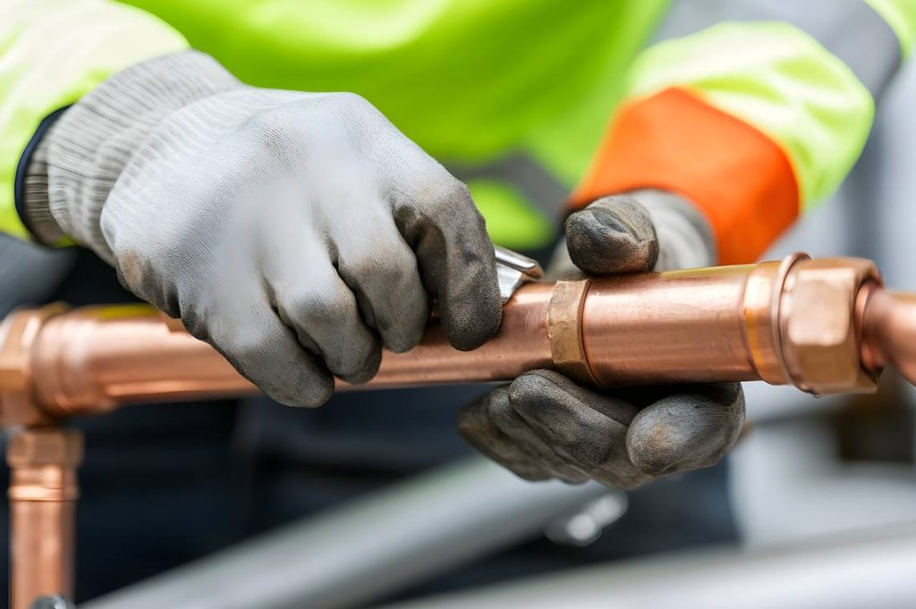 Un professionnel réalise un calorifugeage tuyau de chauffage en ajustant des éléments sur une canalisation en cuivre.