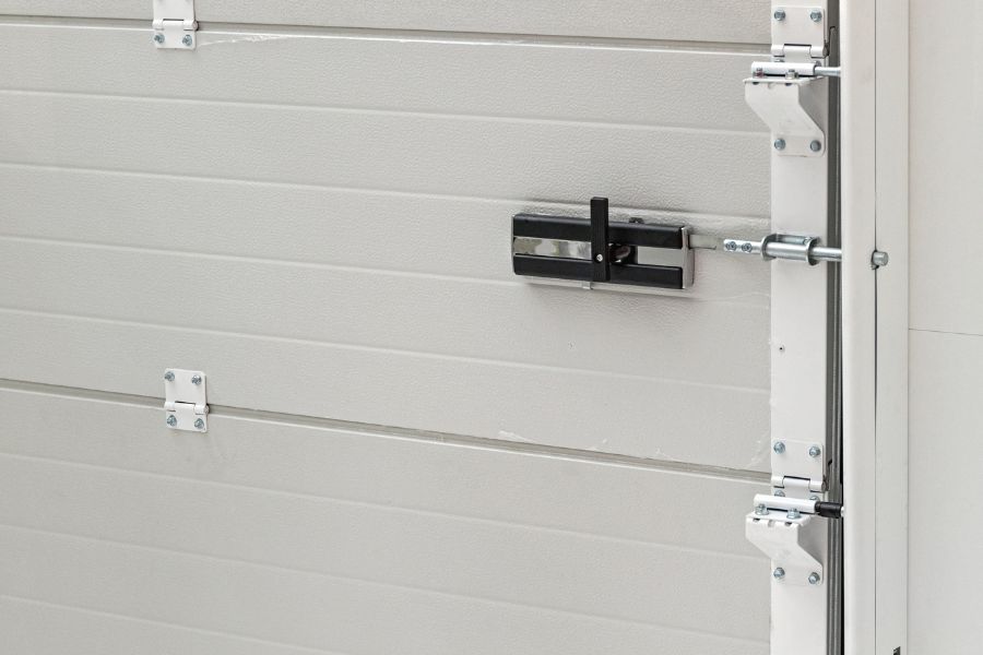 Gros plan sur la poignée de verrouillage et les tringles d'une porte de garage sectionnelle blanche, représentant le cas où la serrure de porte de garage sectionnelle refuse de s'enclencher.